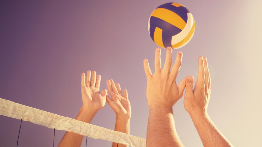 Two pairs of hands above the net going after a volleyball