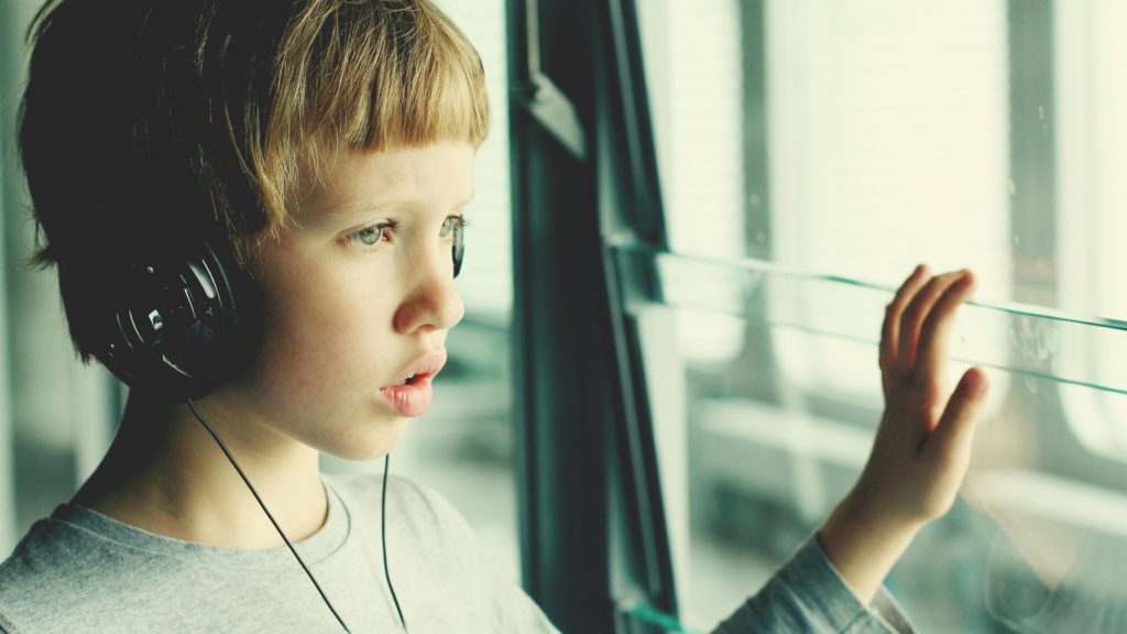 Young boy staring out a window wearing headphones