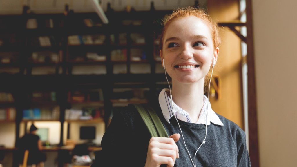 A young red-headed woman smiling inside her school's library