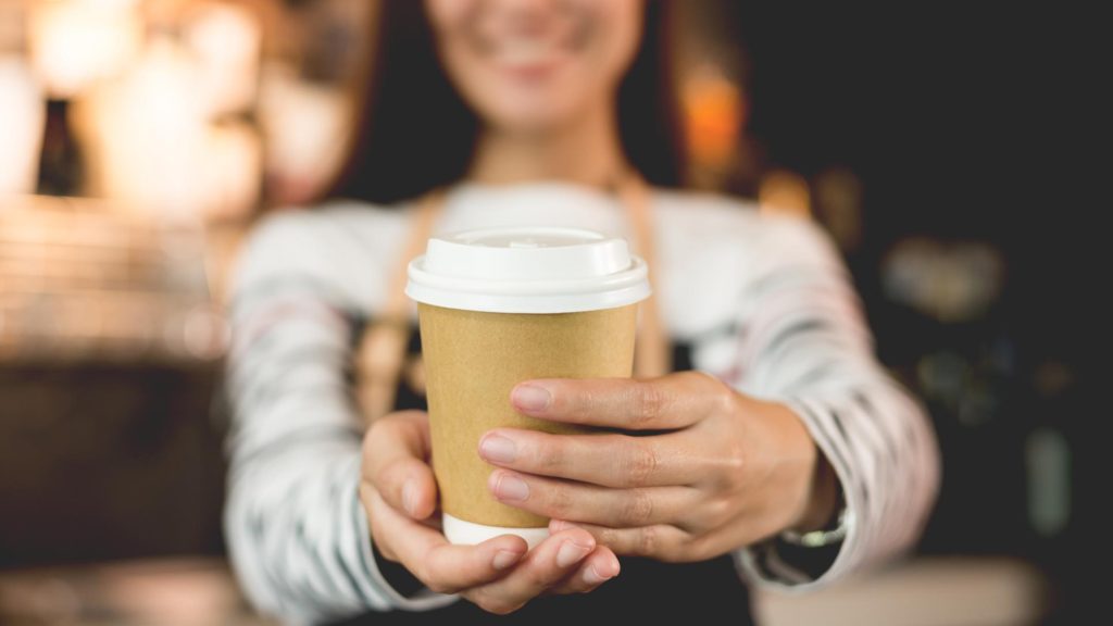 Female barista handing a coffee to you in first-person view