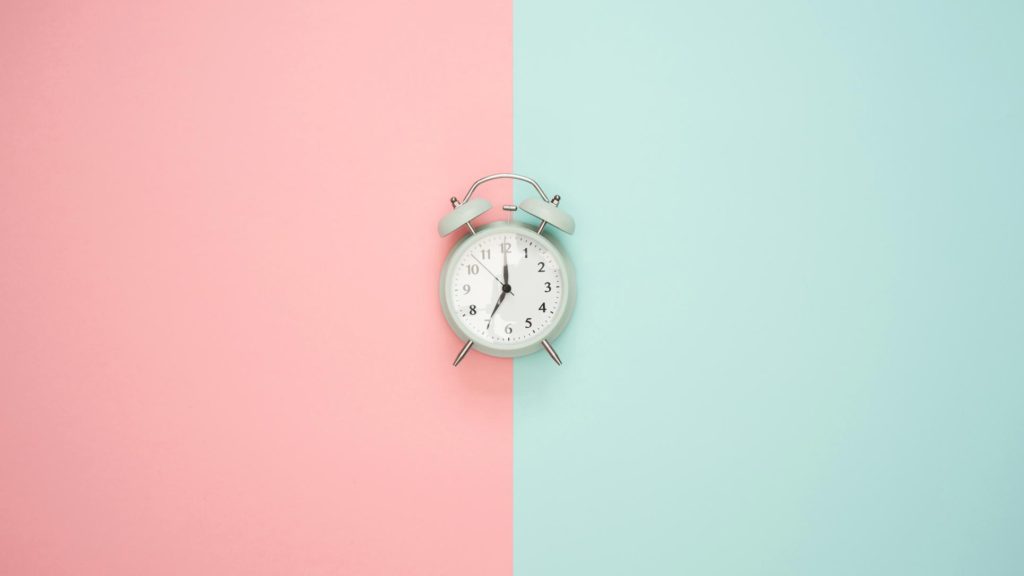 An alarm clock laid on top of a teal and pink background