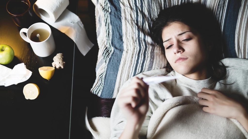 Female in bed checking her temperature on a digital thermometer