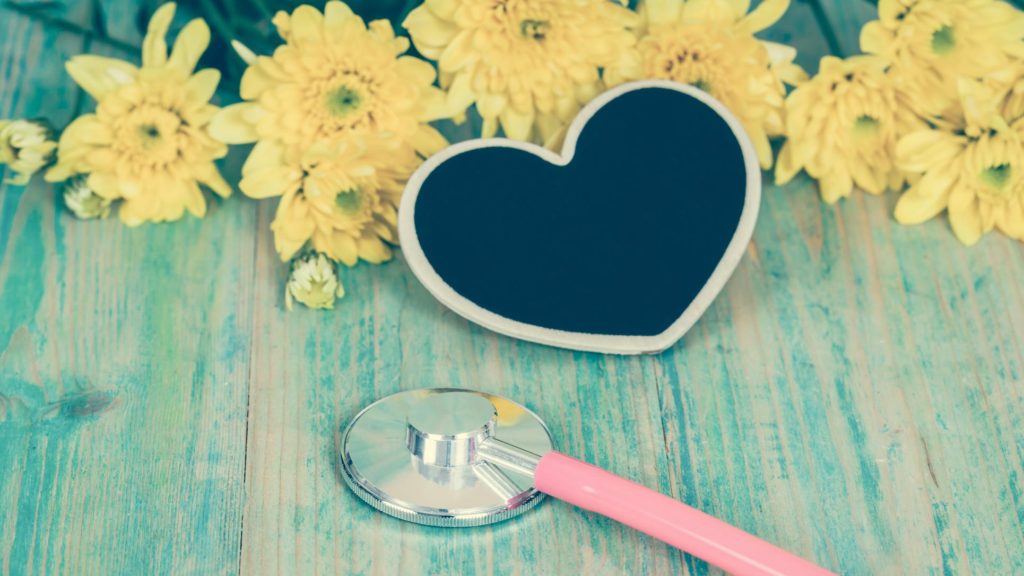 Wooden surface with a heart-shaped decoration, flowers, and stethoscope