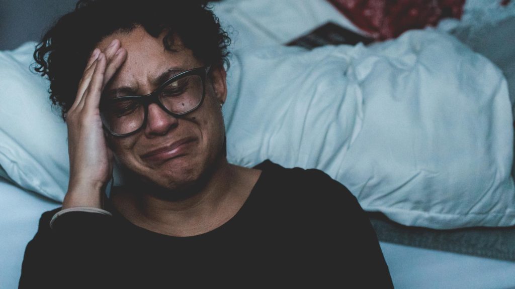 Middle aged African-American woman crying beside a bed