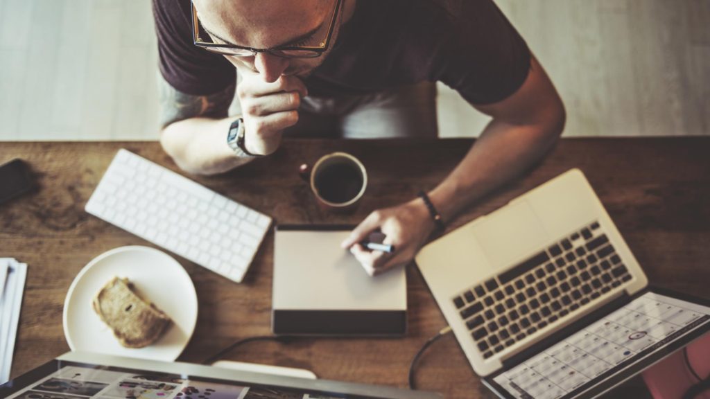 Top down photo of a male intently working from two computers